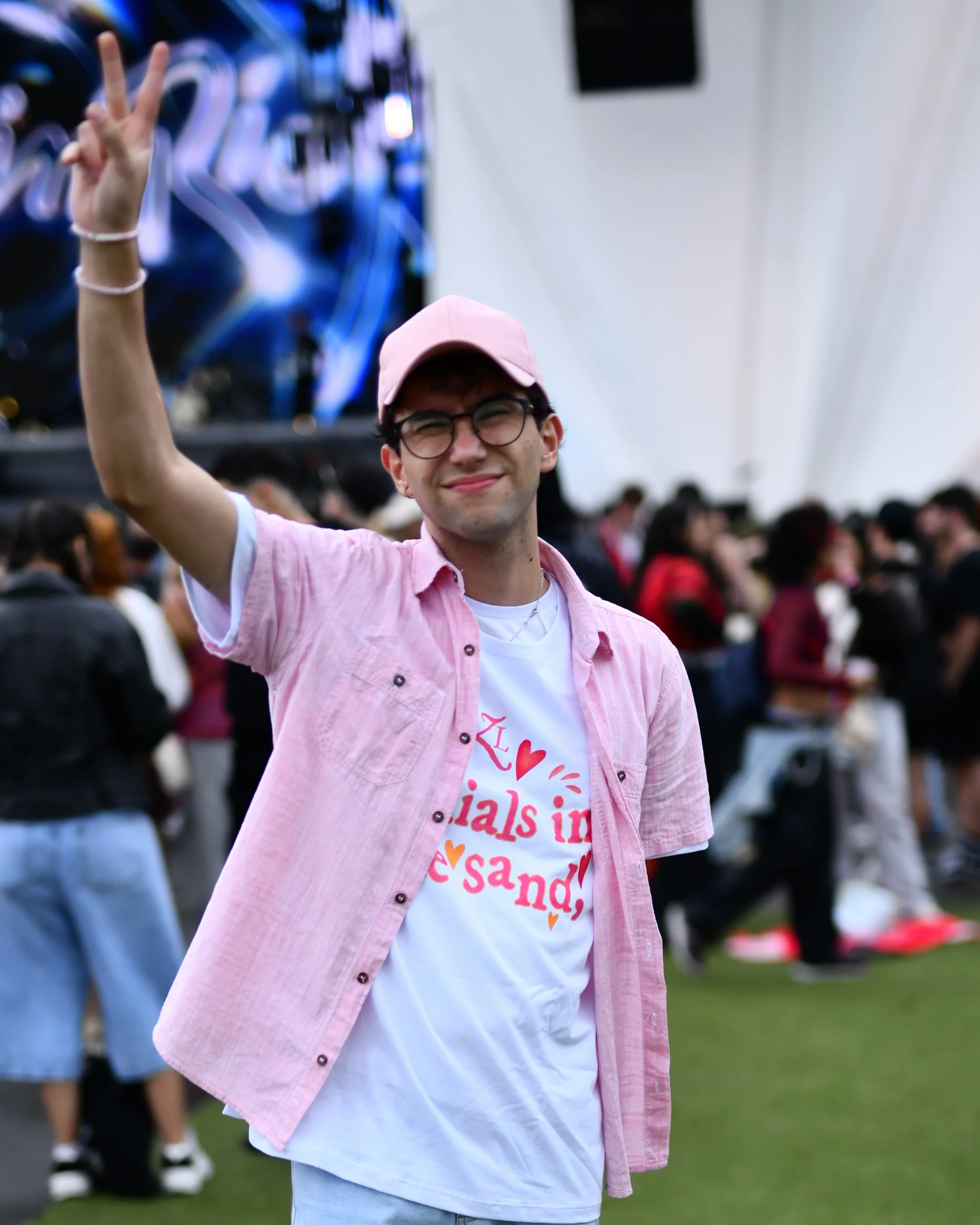 Otávio de boné e camisa rosa fazendo sinal de paz na frente do palco do Rock in Rio